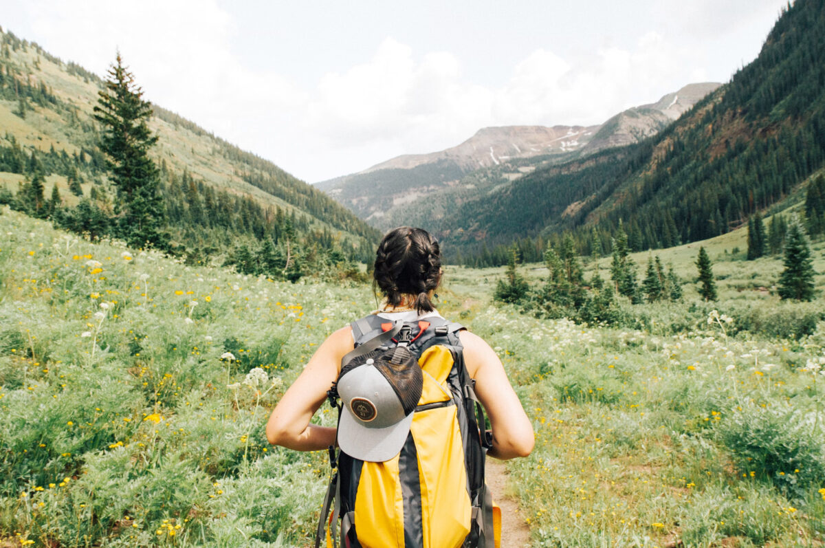 A woman wearing a yellow backpack looks over a mountainscape